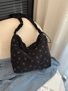 Black corduroy strawberry print tote bag with ruffled strap on a cozy background