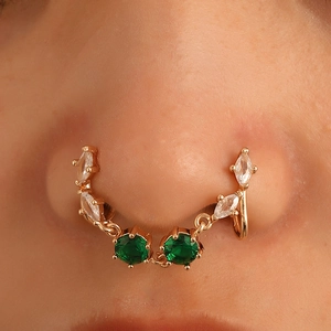 Macro shot of gold U-shaped non-piercing nose clip with emerald green and clear zircon stones