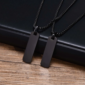 Close-up of dual matte black rectangle pendants on bead chain over leather and wood surface