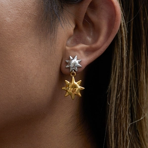 Close-up of two-tone sun pendant earrings with silver and gold finish on a model