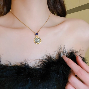 Detail of vintage gold coin pendant necklace with dark blue gemstone on a fine chain