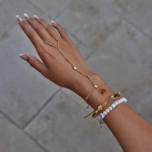 Detail of gold-plated stacked bracelets with cherry charm and porcelain beads on wrist