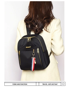 Detail of black oxford backpack featuring gold zippers and a striped charm on white coat