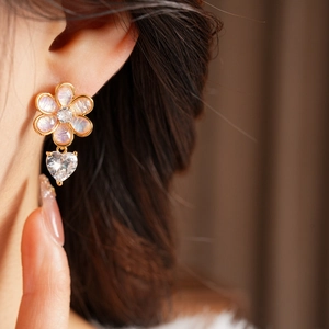 Detail of floral earring with heart-shaped zircon drop worn by model in warm light