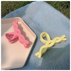 Detailed view of twisted matte hair claws in pastel pink and yellow on outdoor fabric