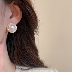 Close-up of elegant vintage-style round pearl stud earrings with gold accents on model