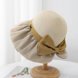 Detailed shot of beige woven straw sun hat with large bow on a wooden stand