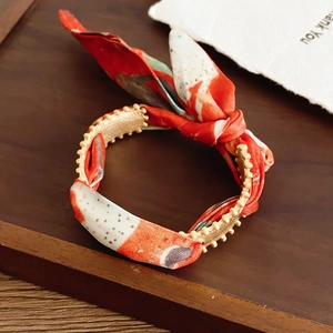 Macro detail of red floral silk scarf fabric tied to a textured golden metal cuff bracelet