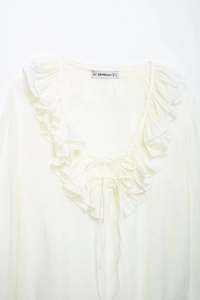 Close-up of the ruffled V-neckline with decorative tie strings on white chiffon blouse