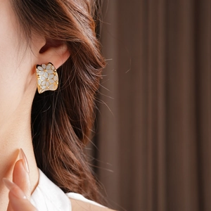 Gros plan d'élégantes boucles d'oreilles fleurs plaquées or avec émail blanc sur un modèle