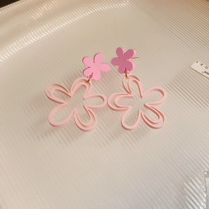 Close-up of pink double-layered acrylic floral stud earrings on a textured tray