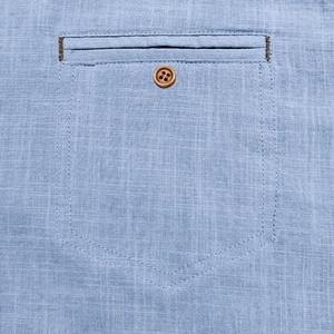 Detailed close-up of a light blue cotton linen shirt pocket with a brown wooden button