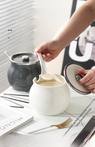 Modern white and grey ceramic seasoning jars with lids and spoons in a kitchen setting