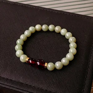 Minimalist Hetian jade beaded bracelet with red accents and golden spacers on dark box