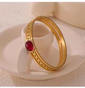 Close-up of gold plated stainless steel bangle with a red oval gemstone on ceramic