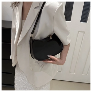 Detail showing a black patent leather underarm bag with zipper on a model's shoulder