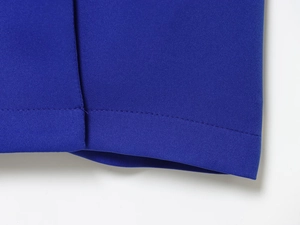 Gros plan sur la texture du tissu bleu roi et les coutures précises sur l'ourlet de la robe