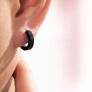 Close-up of matte black stainless steel huggie earring with carbon fiber texture