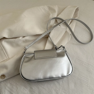 Metallic silver underarm bag with minimalist industrial style on a soft corduroy surface