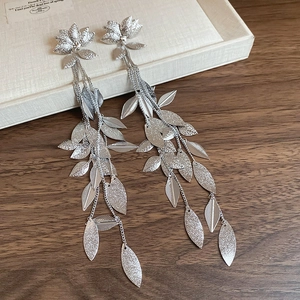 Détail de boucles d'oreilles feuille d'argent avec clous fleurs et longues chaînes
