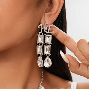 Detail of silver drop earrings featuring letter HE with geometric crystals on model