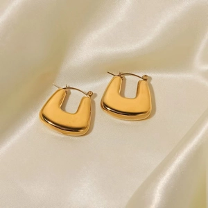 Minimalist gold-polished U-shaped geometric earrings displayed on elegant champagne silk fabric