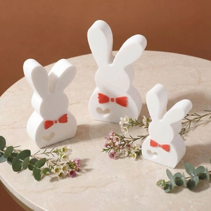 Three white rabbit ornaments with red bows and heart cut-outs on marble table