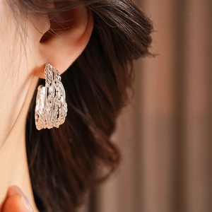 Close-up of a model wearing silver braided C-shaped hoop earrings with woven texture