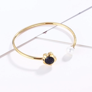 Detail of golden bangle featuring flower blue sandstone charm and white faux pearl accent