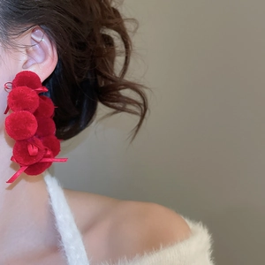 Detail of long red plush ball earrings with ribbons worn on ear with soft white top