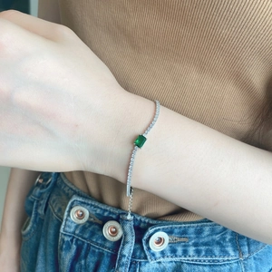 Detail of silver tennis bracelet with green emerald-cut stone and zircon inlay on wrist