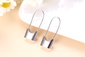 Detailed view of silver safety pin lock earrings on white ceramic tray with floral accents
