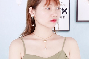 Detail of gold LOVE letter shell necklace and pearl drop earrings on female model
