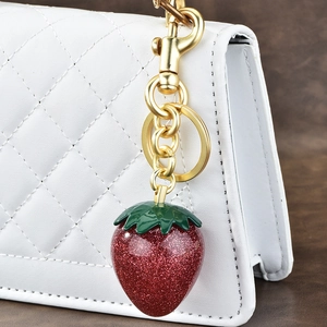Sparkly red strawberry keychain with green leaves on a white quilted bag