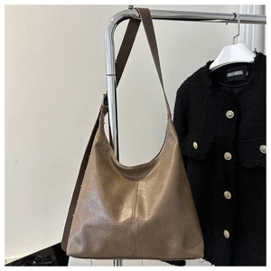 Close-up of a brown leather hobo shoulder bag hanging next to a black tweed jacket