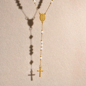 Detailed view of golden Virgin Mary medal and cross pendant with white pearls
