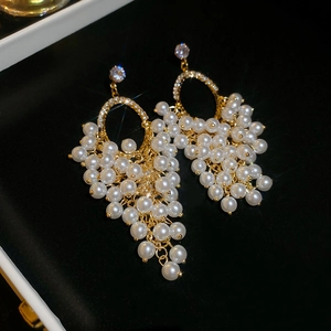 Detail view of pearl grape cluster tassel earrings with gold accents on black velvet background