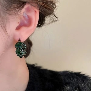 Close-up of vintage-style green crystal earrings worn by model on beige background
