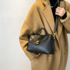 Chic black leather tote bag with gold lock buckle, styled on a camel wool winter coat