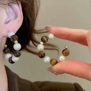 Détail de boucles d'oreilles en C avec perles, œil de tigre et accents dorés