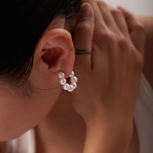 Detail of 18K gold plated C-shaped earrings with large white pearls on a model