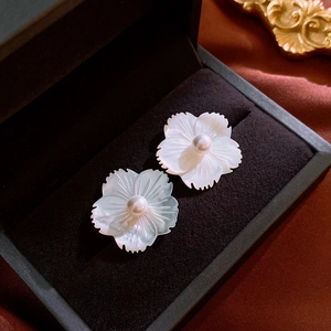 Close-up of elegant flower stud earrings with shell petals and pearls on black velvet