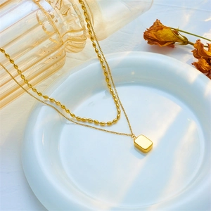 Double-layered gold titanium necklace featuring a square pendant on a white ceramic plate
