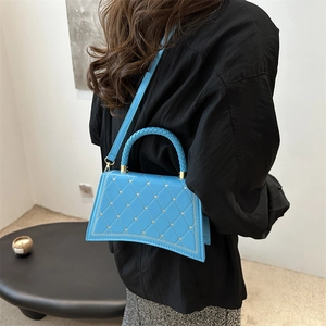 Blue trapezoid handbag with diamond quilting and heart studs on woven handle strap