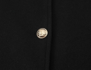 Detailed macro view of a golden metal button on black wool short coat fabric