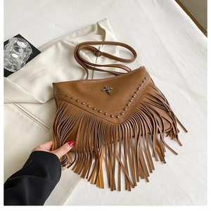 Détail du sac en cuir marron avec rivets argentés, longues franges et emblème de croix