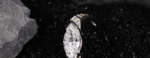 Makroaufnahme von Marquise-Schliff Ring mit Seitendiamanten auf schwarzem Sandstein