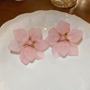 Close-up of pink petal earrings with pearl centers on a white ceramic tray
