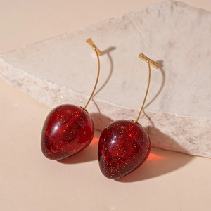 Macro detail of red glitter cherry earrings on a natural stone base with golden stems