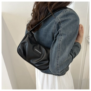 Détail du sac baguette noir plissé porté à l'épaule montrant la taille et la matière